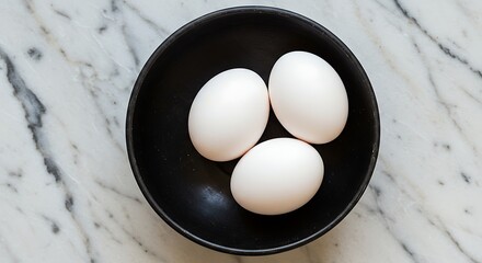 Three white eggs in black bowl on marble surface food photography
