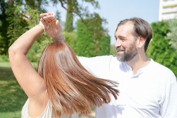 A man and a woman are dancing together in a park. The man is smiling and the woman is laughing