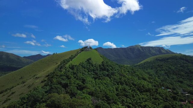 Aerial approach toward green Mount Tapyas above Coron with hilltop cross forested ridges and bright blue sky over Busuanga Island Palawan