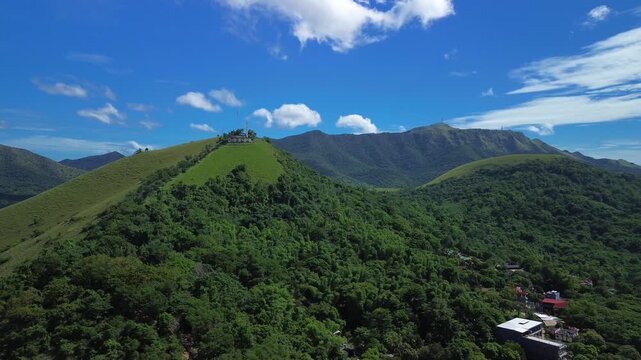 Wide aerial view toward Mount Tapyas above Coron with a green hilltop ridge forested valley distant mountains town rooftops and bright daylight sky in Palawan