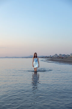 A woman stands in the water at the beach during dawn
