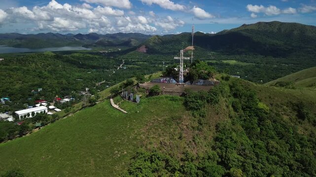 Aerial view over the Mount Tapyas summit in Coron showing the hilltop cross Coron letters green ridges town edge distant bay and layered mountain valley