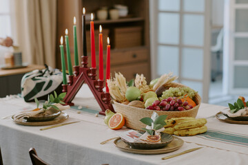 Kwanzaa kinara with seven lit candles standing on dining table surrounded by basket of assorted fruits and vegetables, traditional holiday setting celebrating heritage
