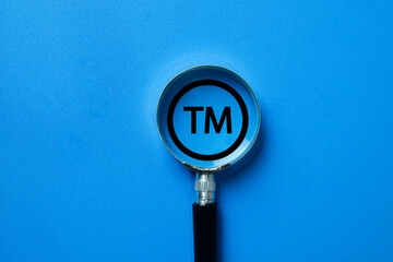A magnifying glass focusing on a Trademark (TM) symbol. A concept for intellectual property (IP)...