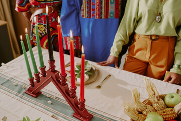 Fototapeta premium Three people standing around table with kinara holding seven candles, celebrating Kwanzaa, visible hands and torsos suggesting young adult and middle aged Black women and man