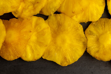 dried ripe bright yellow pineapple on a black slate board, cut into rings and dried yellow clean slices of ripe pineapple for long-term storage and used as a sweet