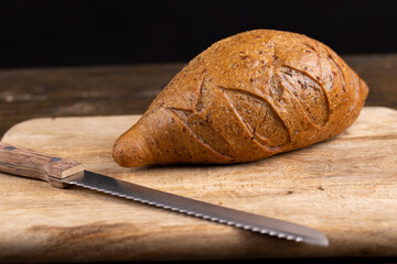 a whole small loaf of rye flour bread lies on the table on a cutting board, a small loaf of freshly...