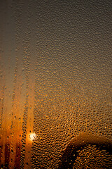 Obraz premium water droplets from condensation on the window glass at sunset, wet glass with water droplets on the background of an orange sky out of focus at sunset