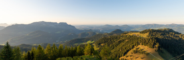 Panoramic alpine landscape with rolling hills, forested ridges and distant valleys in warm evening light