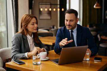 Business colleagues working on laptop during meeting in cafe.
