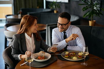 Happy colleagues using smart phone during business lunch in restaurant.