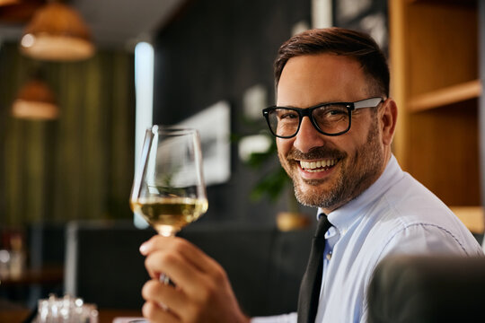 Happy businessman having glass of wine in restaurant and looking at camera.