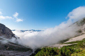 Obraz premium Cloud inversion drifting through rugged alpine landscape under clear blue sky