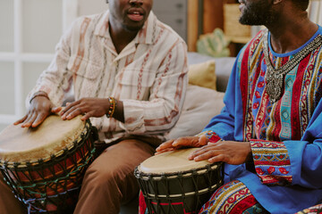 Two Black men playing traditional drums during Kwanzaa celebration, sitting side by side, focusing...