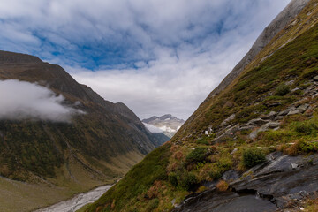 Moody alpine valley trail in the Zillertal Alps, dramatic clouds rolling through green mountain slopes, remote hiking landscape with changing weather in the Austrian Alps