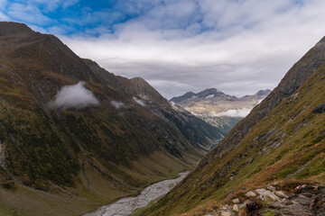 Moody alpine valley trail in the Zillertal Alps, dramatic clouds rolling through green mountain slopes, remote hiking landscape with changing weather in the Austrian Alps