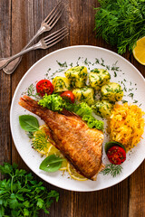 Fried atlantic redfish with boiled potatoes and sauerkraut on wooden table. Top view