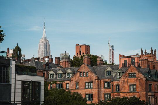 View of the Empire State Building standing tall behind the brick buildings and lush greenery under a clear blue sky, New York, New York, United States.