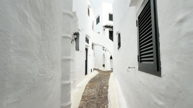 A narrow alleyway with a stone path and a white building in binibeca menorca