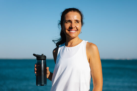 Fototapeta Smiling woman enjoys outdoors with a water bottle by the sea
