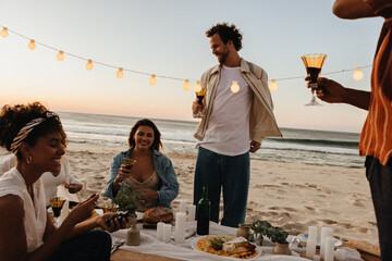 Friends sharing a joyful moment with drinks on a beach during sunset