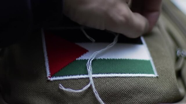Close-up of a hand sewing the flag of Palestine onto a fabric