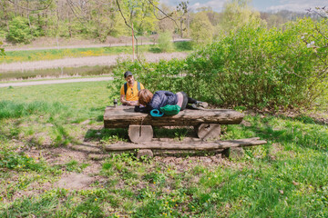 Obraz premium Couple relaxing on a rustic wooden bench in a sunny park with a pond and lush greenery. Perfect for depicting leisure, outdoor adventures, and serene nature breaks.