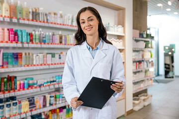 Female pharmacist in white coat holding clipboard while standing in pharmacy