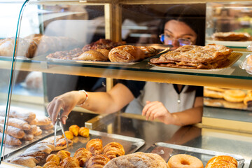 Woman serving croissants in bakery display case