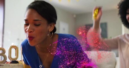 Birthday celebrant blowing candles on cake, generating digital confetti swirling around friends - Powered by Adobe