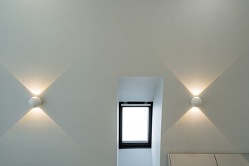 The room features a captivating window that draws the eye, as well as two elegant wallmounted light...