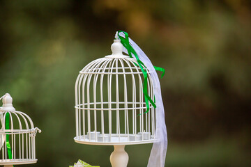 A decorative white vintage-style birdcage adorned with ribbons, used as a centerpiece for a wedding or garden party. A symbol of celebration and romance.