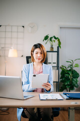 Confident Asian businesswoman multitasking with tablet and laptop in bright office. Ideal for business, technology, consulting, digital work, leadership