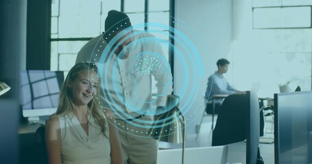 Man tapping smartwatch summoning hologram rings, woman typing analyzing data in business office - Powered by Adobe