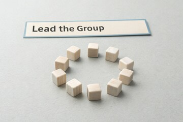 Wooden blocks arranged in a circle with a sign saying 'Lead the Group' on a neutral background