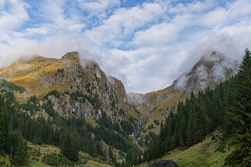 mountain landscape with two big main peaks in front an vertical forest and rainy clouds on blue sky