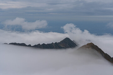 view of highest peaks of romanian carpathian ridge chain from top on very cloudy day with fluffy white clouds at bottom