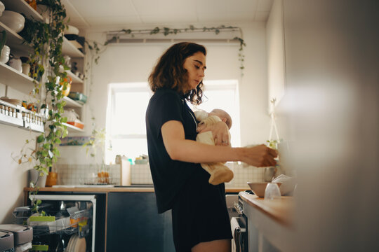 Mother multitasking in kitchen while preparing meal with baby
