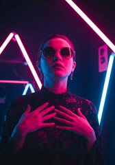 Stylish woman wearing sunglasses and a black lace top, illuminated by vibrant pink and blue neon lights in a dark, atmospheric setting