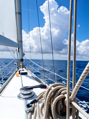 Sailboat sailing on a sunny day, ropes and winches in focus, with ocean and clouds in background