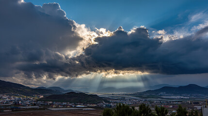 darkness. Beam of sunlight breaking through dark storm clouds, illuminating the ground. travel magazines, destination branding, designed for outdoor magazines and nature guides.
