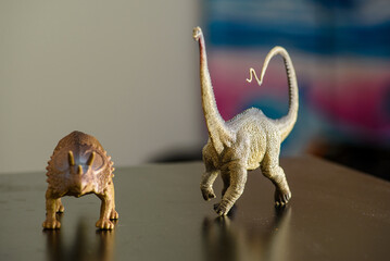 Two figures of Triceratops and Diplodocus dinosaurs on a black table that children like to play with and remind us of the creatures that once lived on Earth
