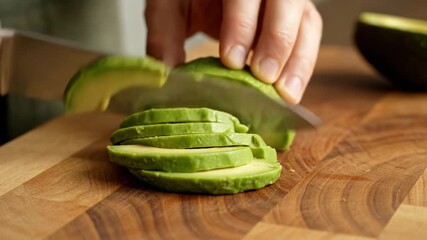 Slicing fresh avocado on wooden cutting board with sharp knife highlights vibrant green color and smooth texture, showcasing culinary skills in healthy food preparation techniques