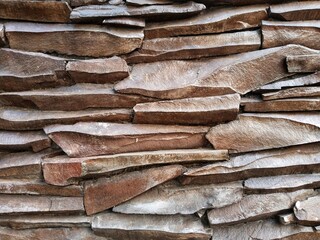 Close-up of a wall surface that features pieces of flat natural stone, such as slate or river stone, which are split-faced or chiseled in texture, arranged horizontally in layers, dark brown in color