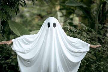 A young boy dressed as a ghost for Halloween wears a white sheet with two black eye holes. He...