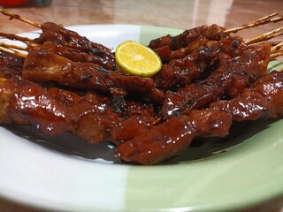 A close-up photo shows delicious Indonesian chicken satay skewers served on a plate with sweet soy sauce glaze and fresh lime garnish.