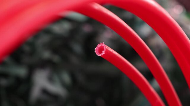 A close-up view of a red plastic tube with a rough cut edge, highlighting its hollow cylindrical form, texture, and industrial synthetic material detail