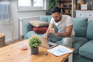 Young university student, freelancer business man, working at home on laptop computer, testing new innovative technology and online internet tools while sitting in home office.