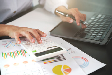 Close-up of hands using calculator and laptop with financial charts on desk office