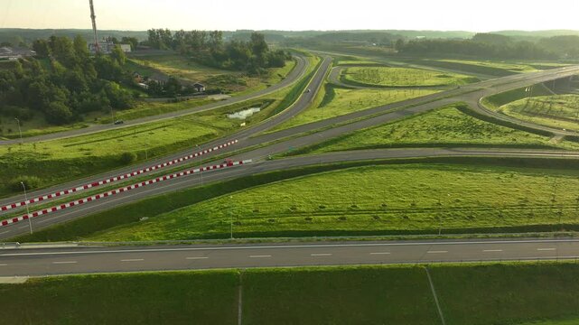 Wide aerial view of a modern highway interchange (S6) near Gdynia, surrounded by incredibly lush green slopes and hills, bathed in golden morning light